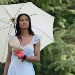 Sonya in a light blue dress and glove holding an umbrella and a sack of bird food.