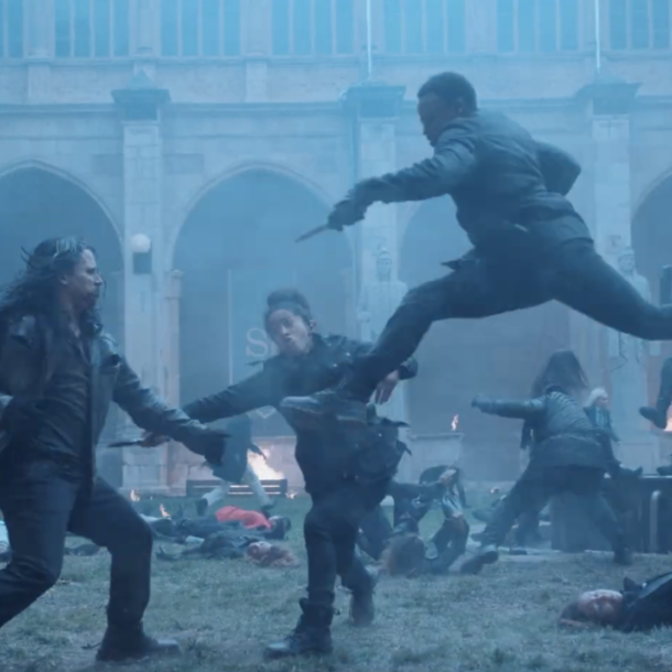 Scene at St. Jude with blue, hazy background. Janine Hathaway leaping through the air during the strigoi attack with her stake pointed at one and another Guardian behind the same strigoi striking forward